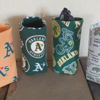 Photo of 4 different upright cylindrical upright eyeglasses holders: Gold with green As with a red heart instead of an apostrophe; green with circular A's logo; green with all over scattered A's logos, elephants and the word Oakland; and white with various A's words and sayings.