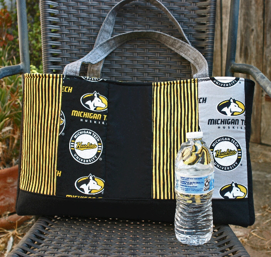 Front view. Vertical strips of MTU and coordinating fabrics. Grey straps. Water bottle (not included) to show size of bag.