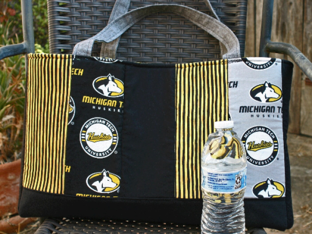Front view. Vertical strips of MTU and coordinating fabrics. Grey straps. Water bottle (not included) to show size of bag.